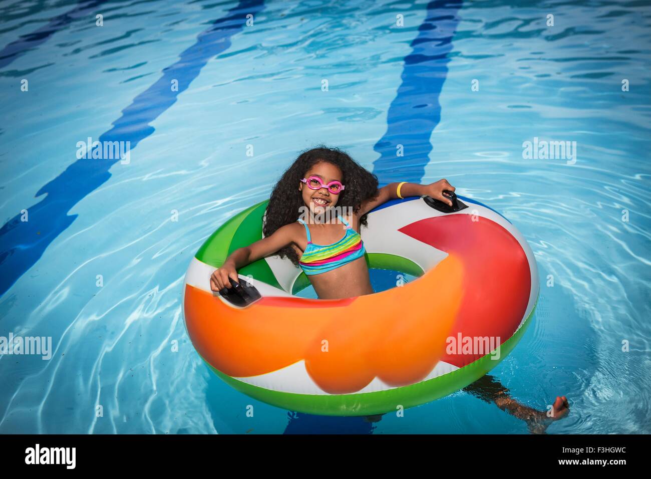 Girl sitting in inflatable ring in swimming pool looking at camera smiling Stock Photo