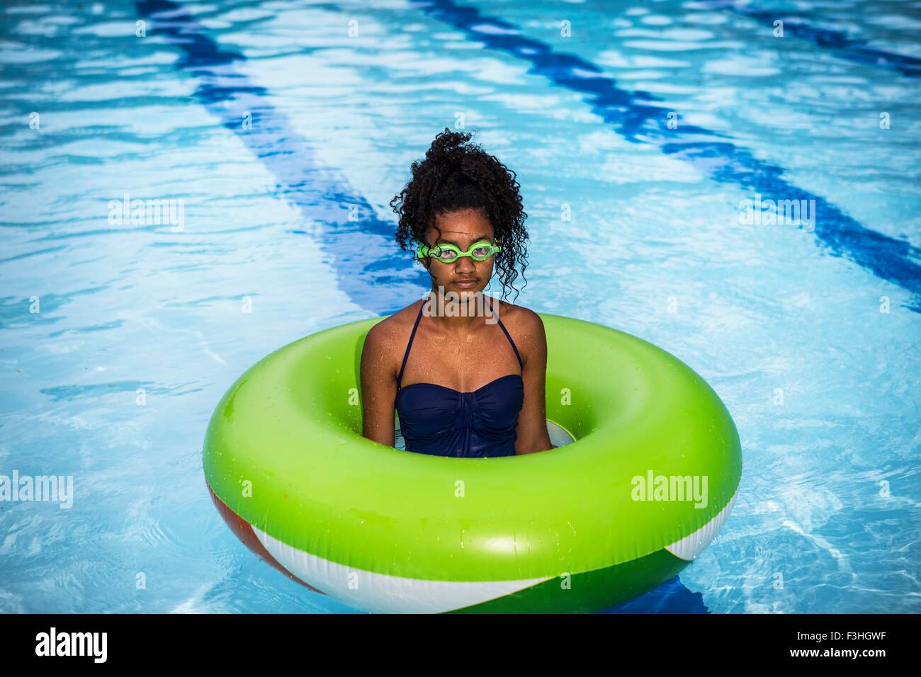 Girl standing in inflatable ring in swimming pool, wearing goggles looking at camera Stock Photo