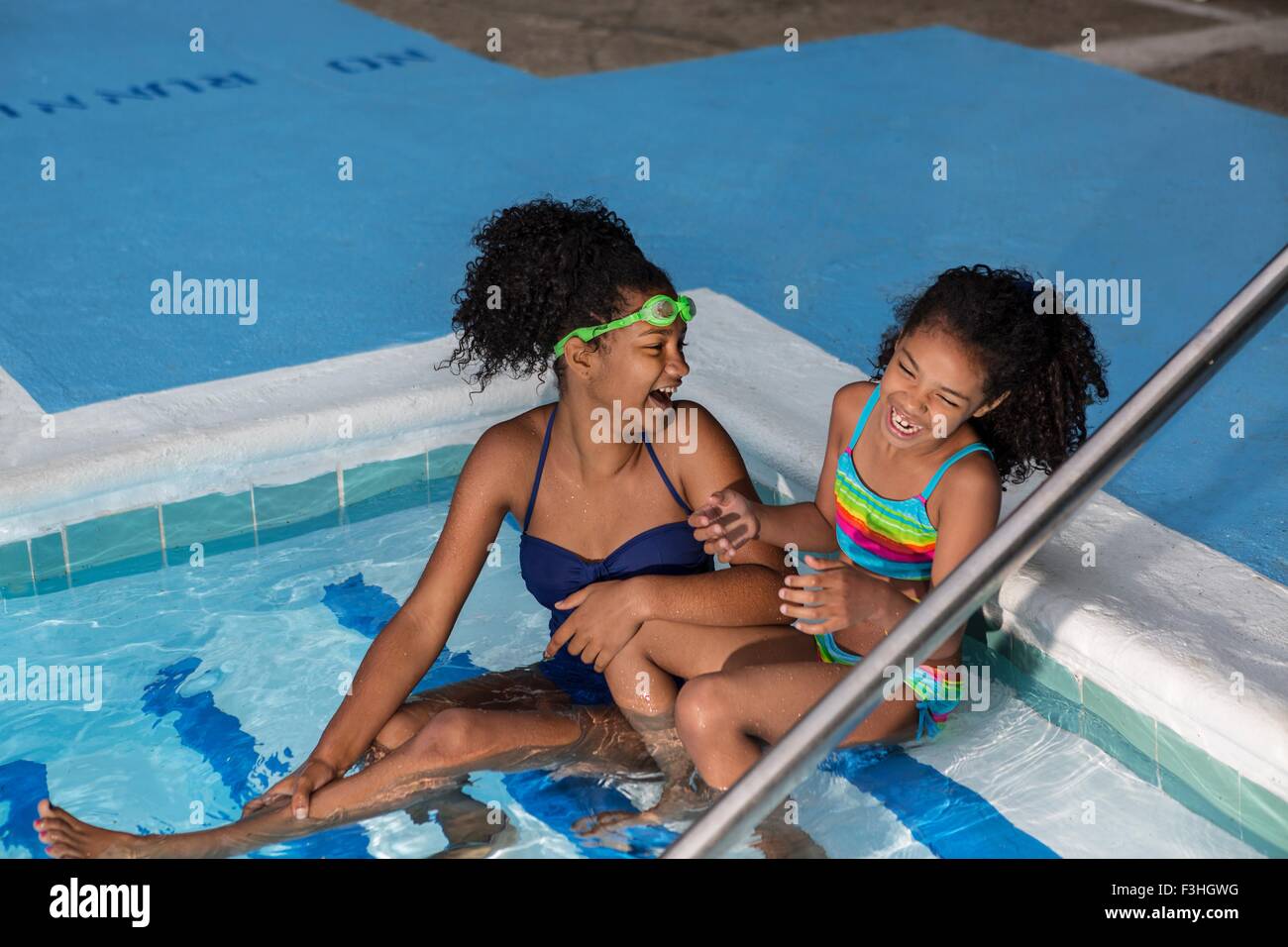 High angle view of girls sitting in swimming pool side by side laughing Stock Photo