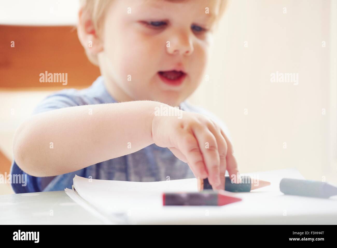 Boy sitting at table touching crayon, focus on foreground Stock Photo