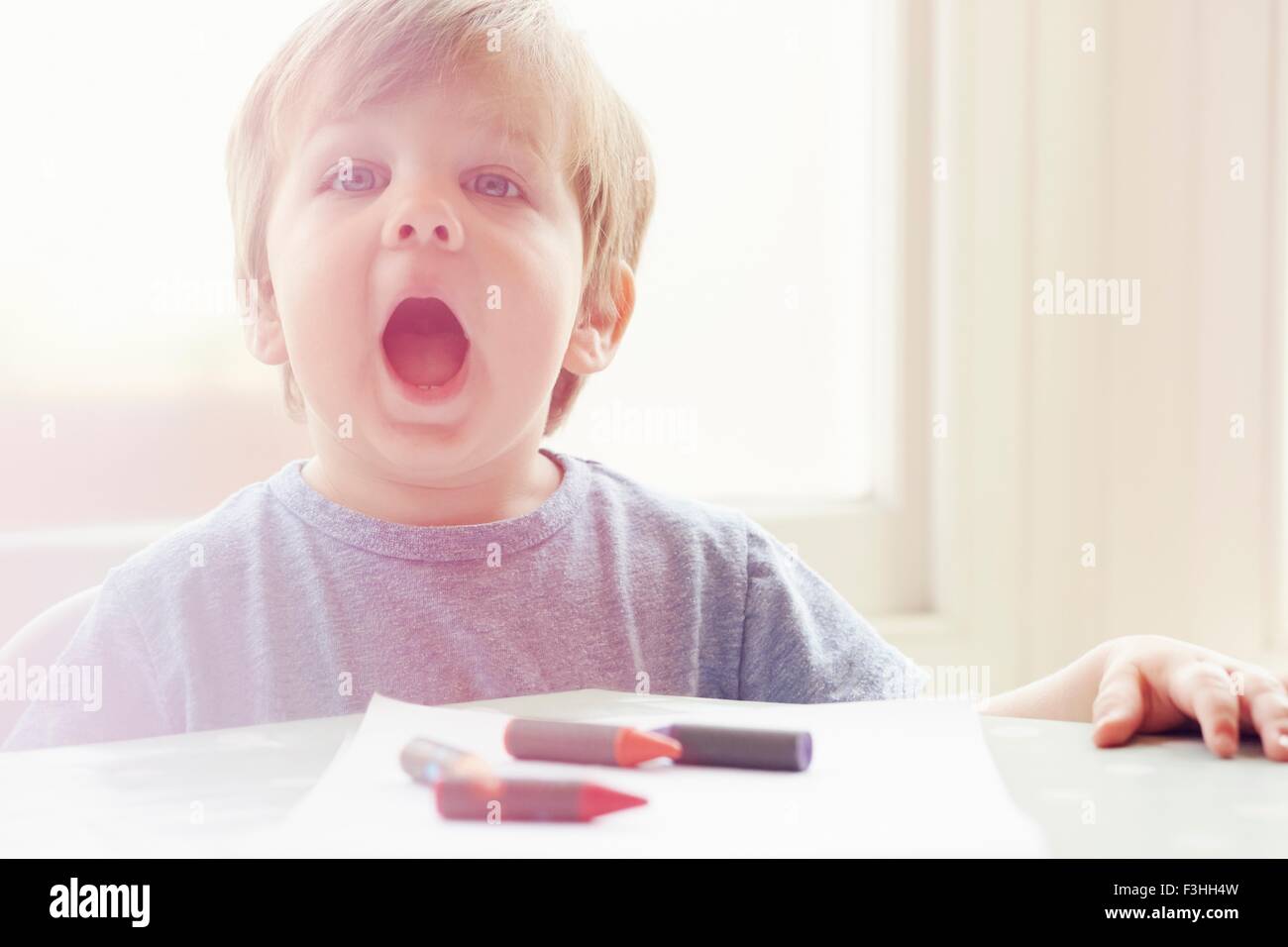 Boy at table with crayons, looking at camera, open mouthed Stock Photo