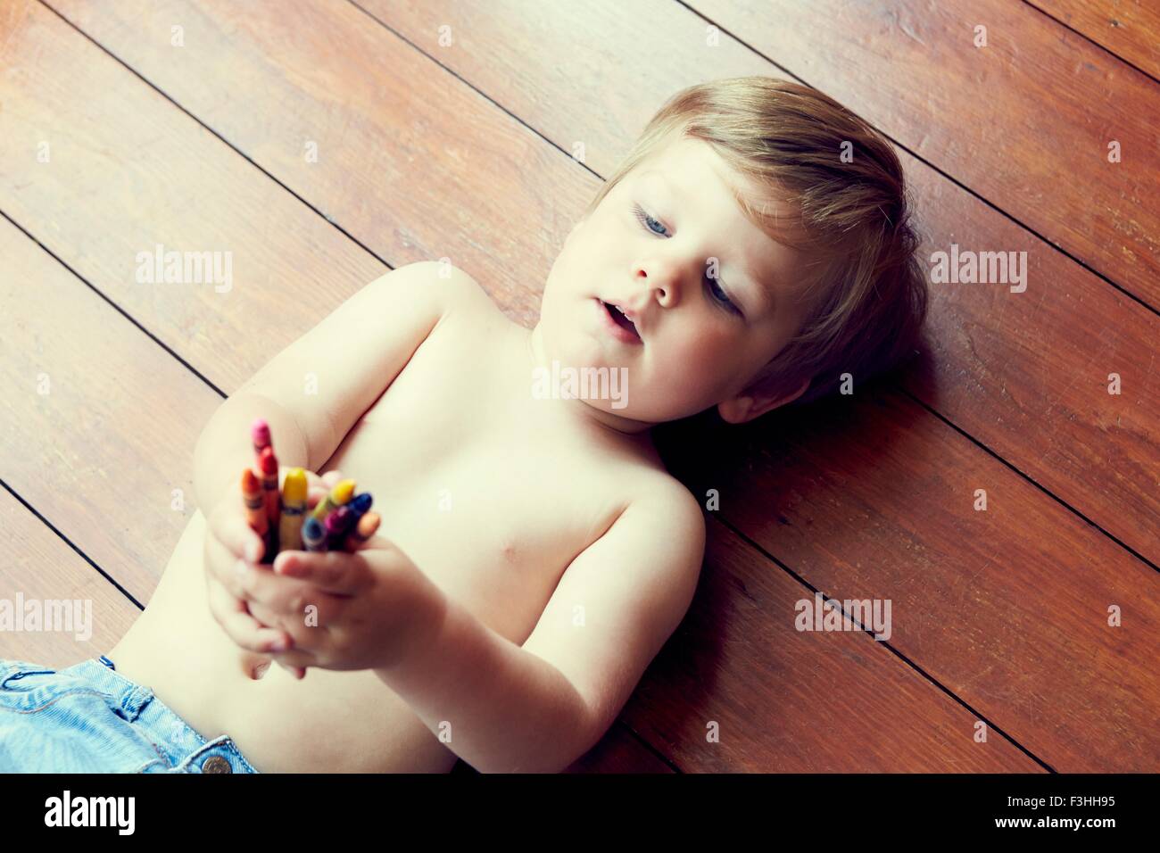 High angle view of boy lying on back on wooden floor holding crayons Stock Photo