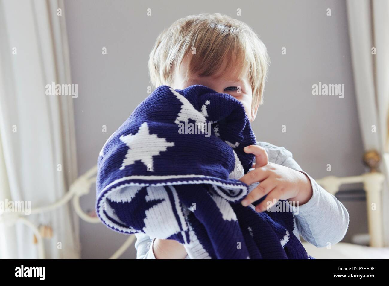 Boy on bed hiding behind navy blue star patterned woollen blanket Stock Photo