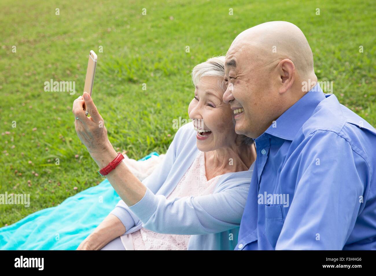 Senior couple sitting in park, taking self portrait using smartphone Stock Photo