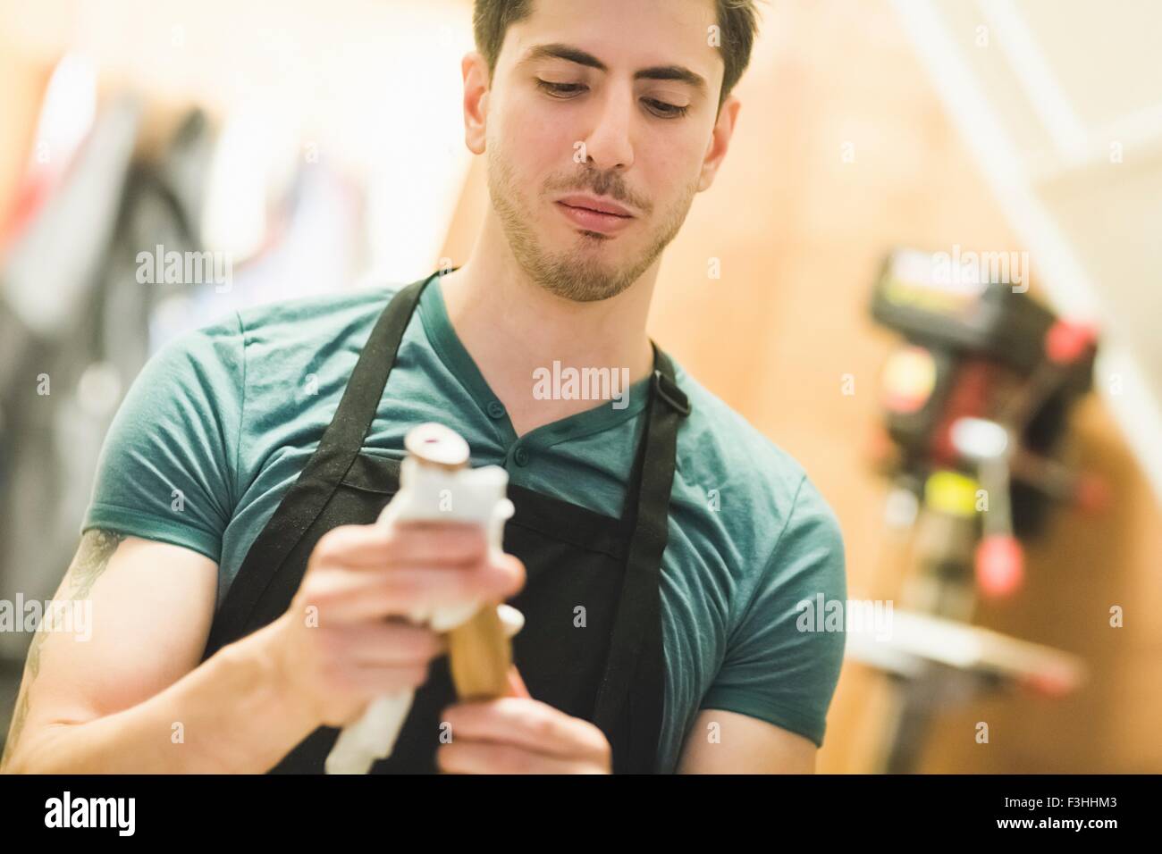 Young man wearing apron crafting wood object, looking down Stock Photo