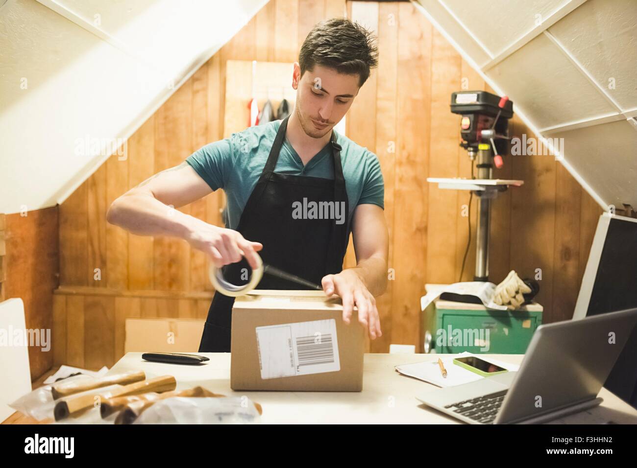 Young man using sticking tape to prepare package for delivery Stock Photo