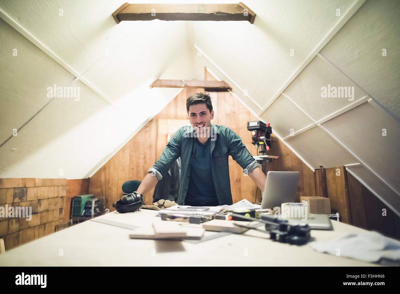 Young man leaning against desk in workshop looking at camera smiling Stock Photo