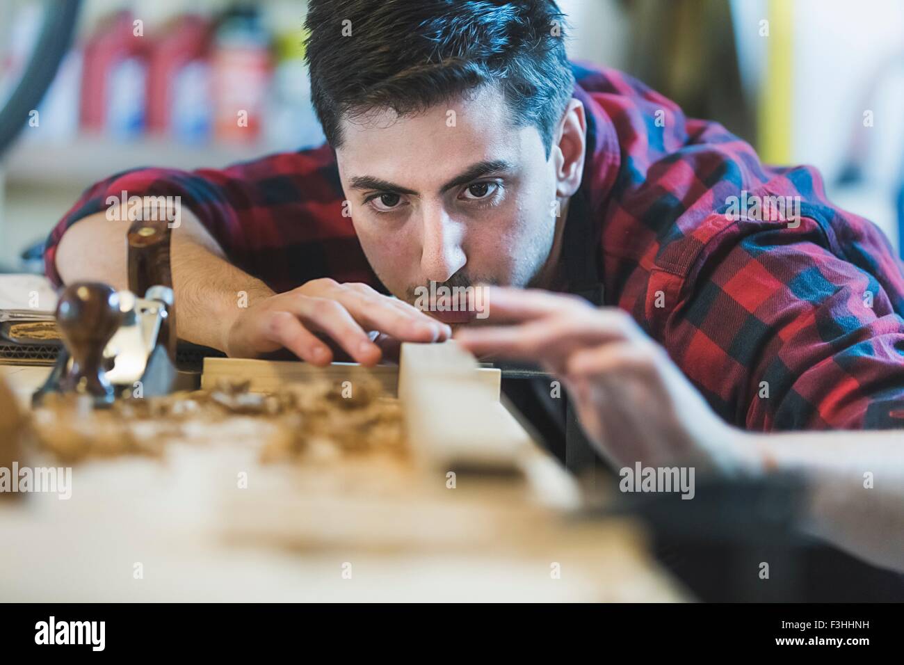 Young man using wood plane to smooth wood object Stock Photo