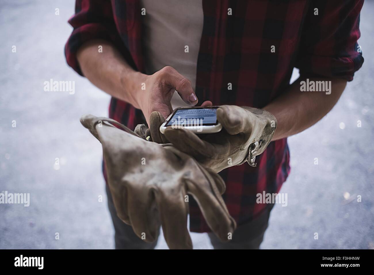 High angle cropped view of young mans hands wearing protective gloves using smartphone Stock Photo