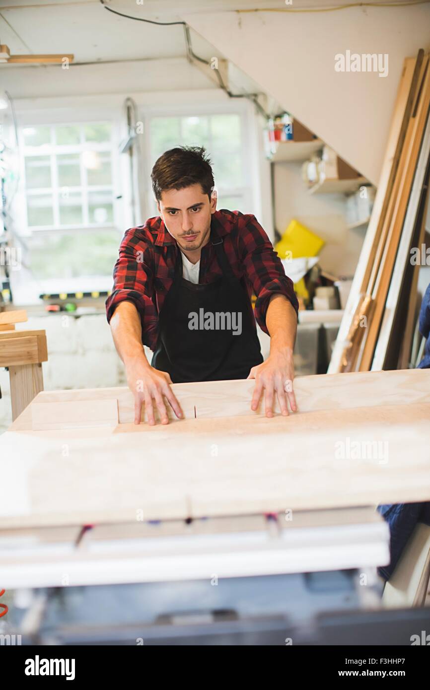 Young man in workshop wearing apron using table saw to cut wood Stock Photo