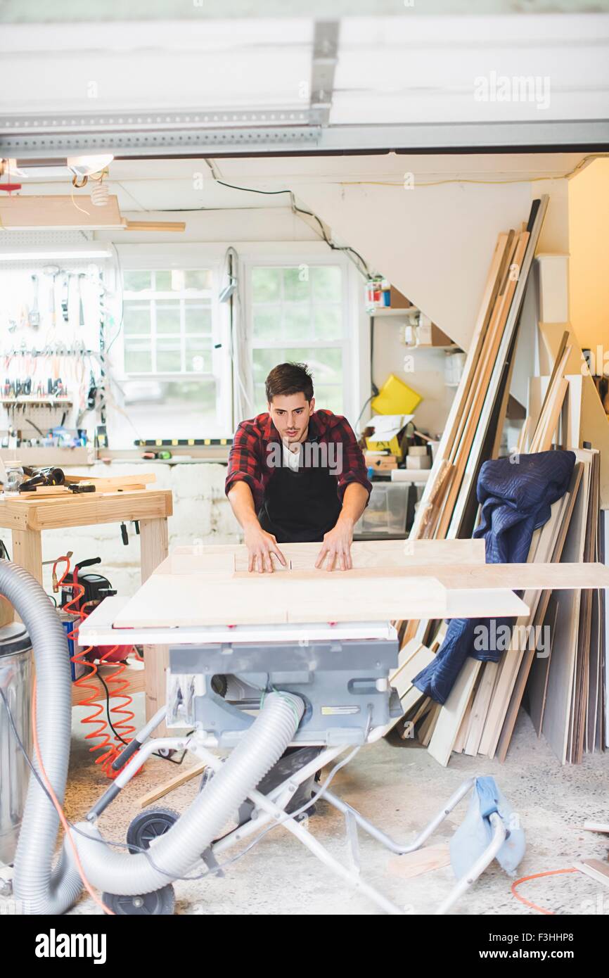 Young man in workshop wearing apron using table saw to cut wood Stock Photo
