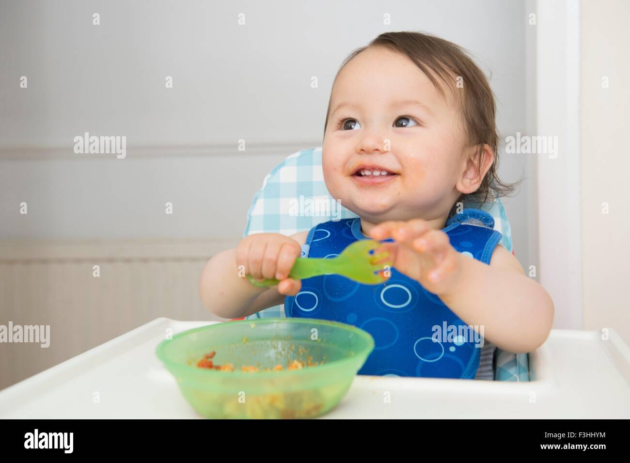 Baby boy eating baby food in kitchen high chair Stock Photo Alamy
