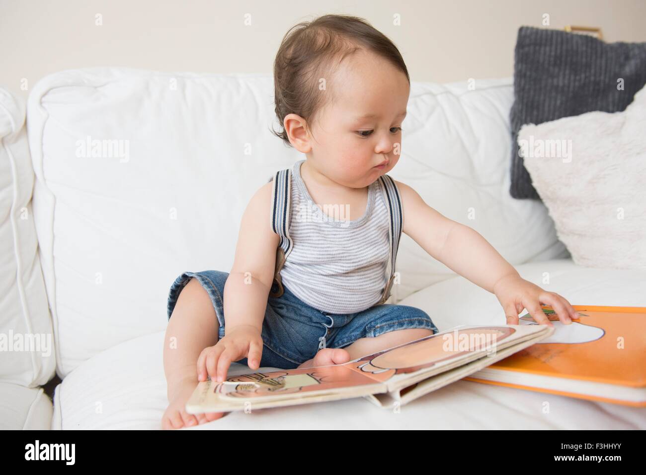 Baby boy sitting on sofa looking at picture book Stock Photo - Alamy