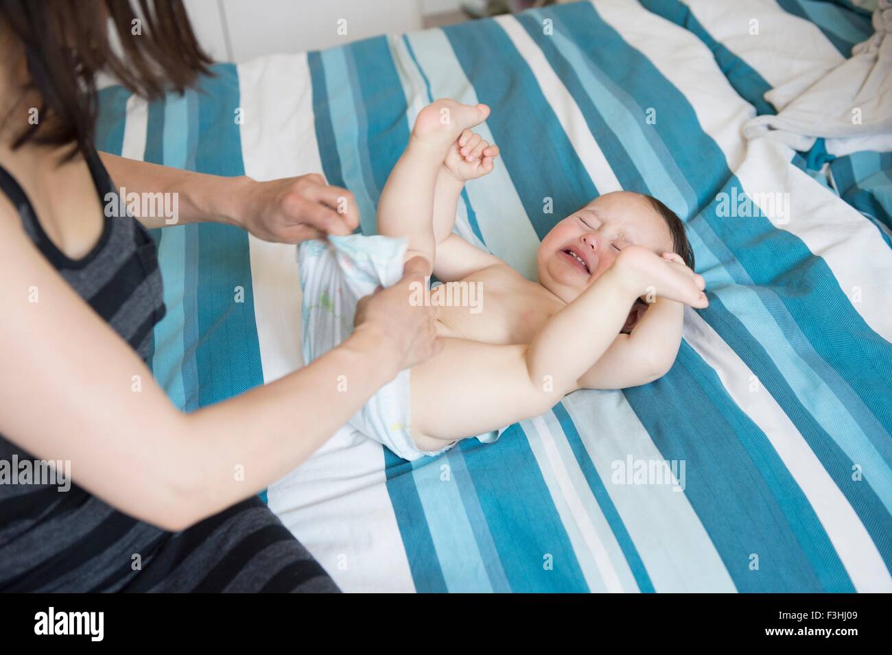 Mature mother changing baby sons nappy on bed Stock Photo