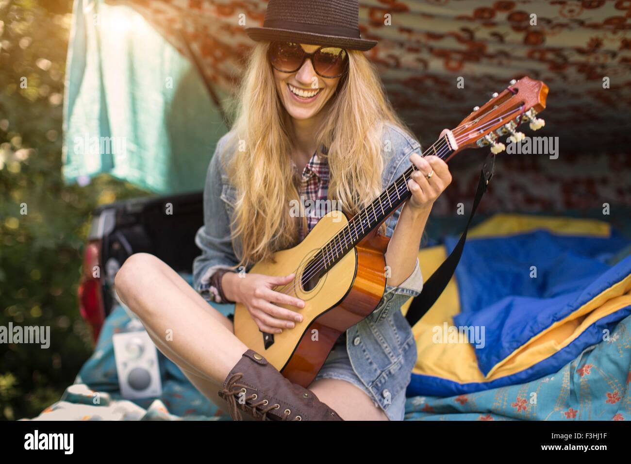 Portrait of young woman playing ukulele whilst camping in pick up boot Stock Photo