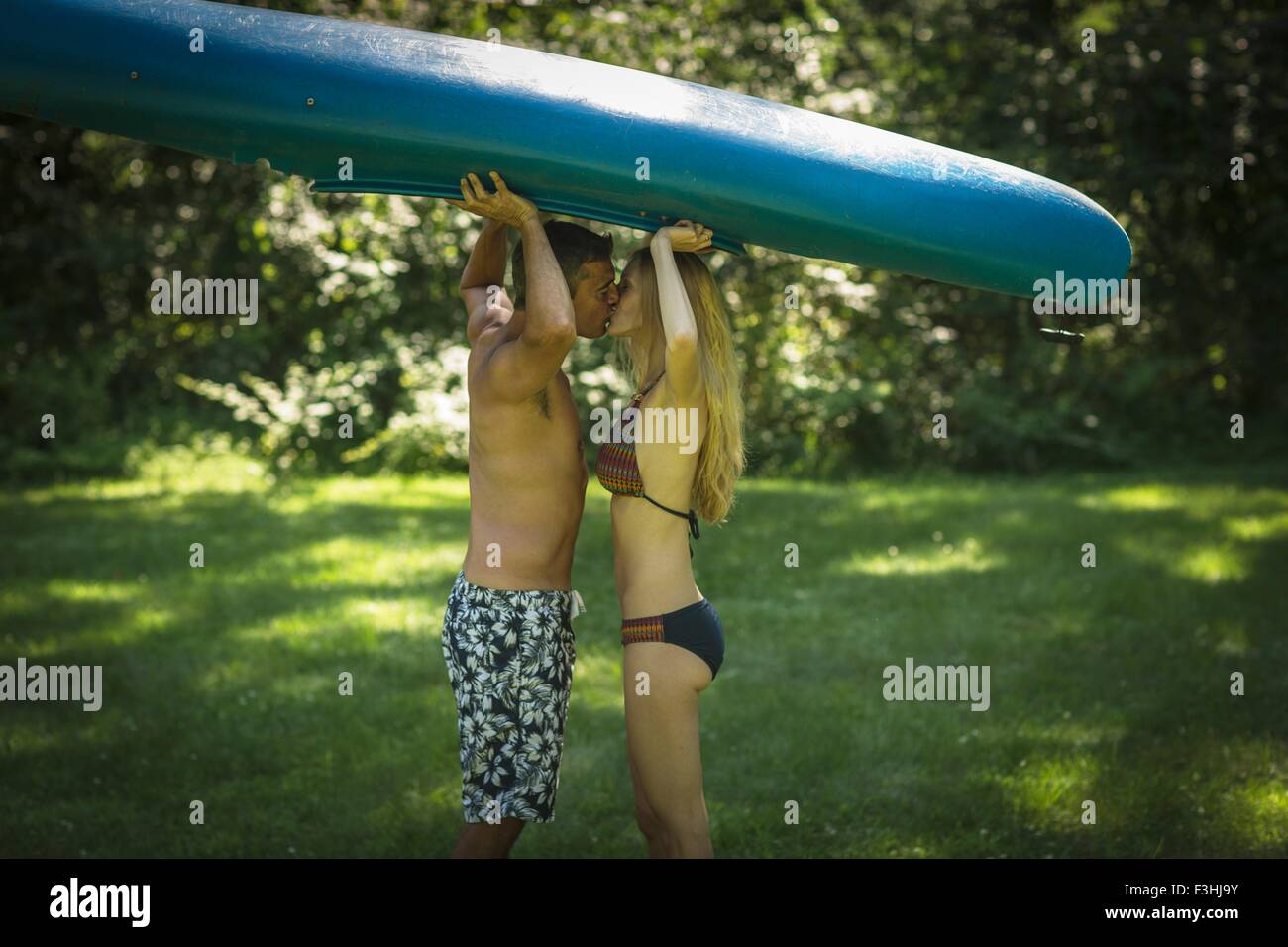 Romantic mature man kissing girlfriend whilst holding up kayak in garden Stock Photo