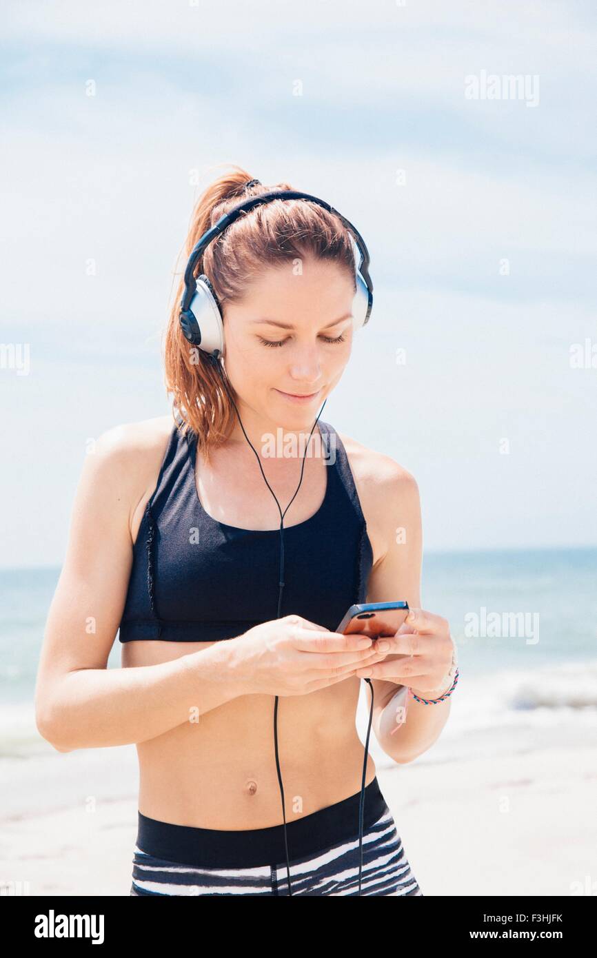 Mid adult woman standing on beach, wearing headphones, looking at mp3 player Stock Photo