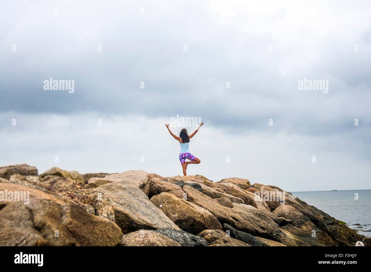 Rear view of mature woman practicing yoga on coastal rocks, Stock Photo