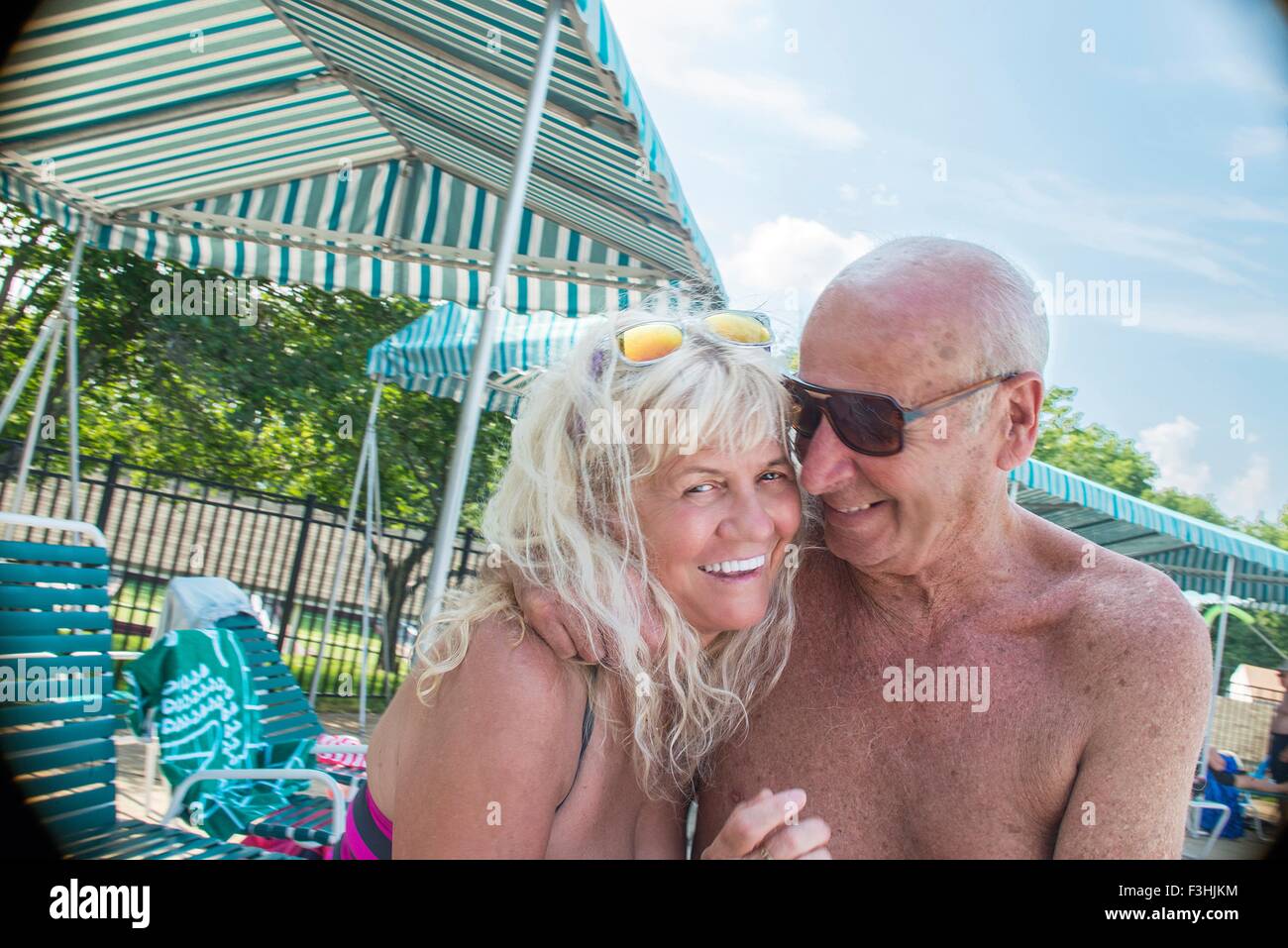 Portrait of affectionate senior couple sitting poolside at outdoor swimming pool Stock Photo