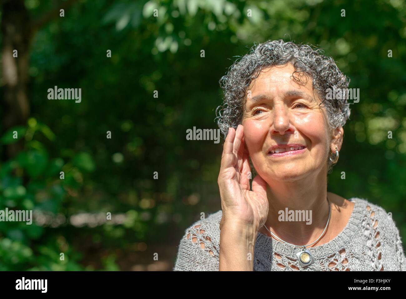 Senior woman with hand on face in park Stock Photo