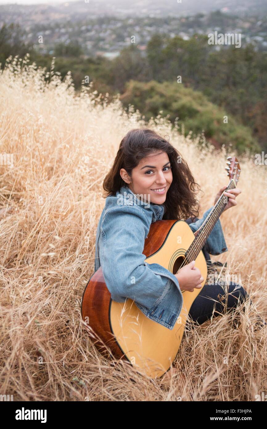 Portrait of young woman playing acoustic guitar on grassy hill Stock ...