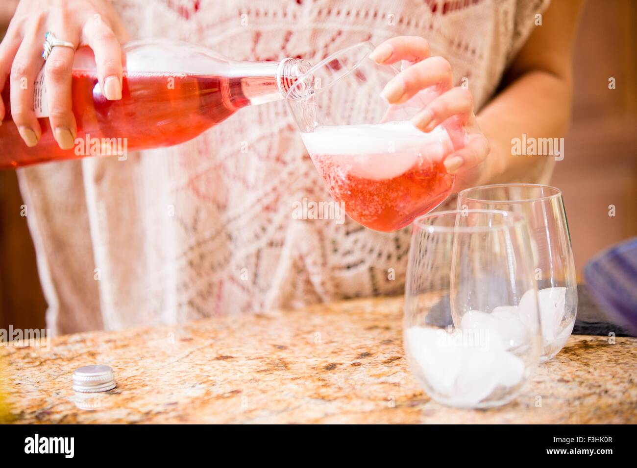 Close up of young woman pouring rose wine at kitchen counter Stock Photo