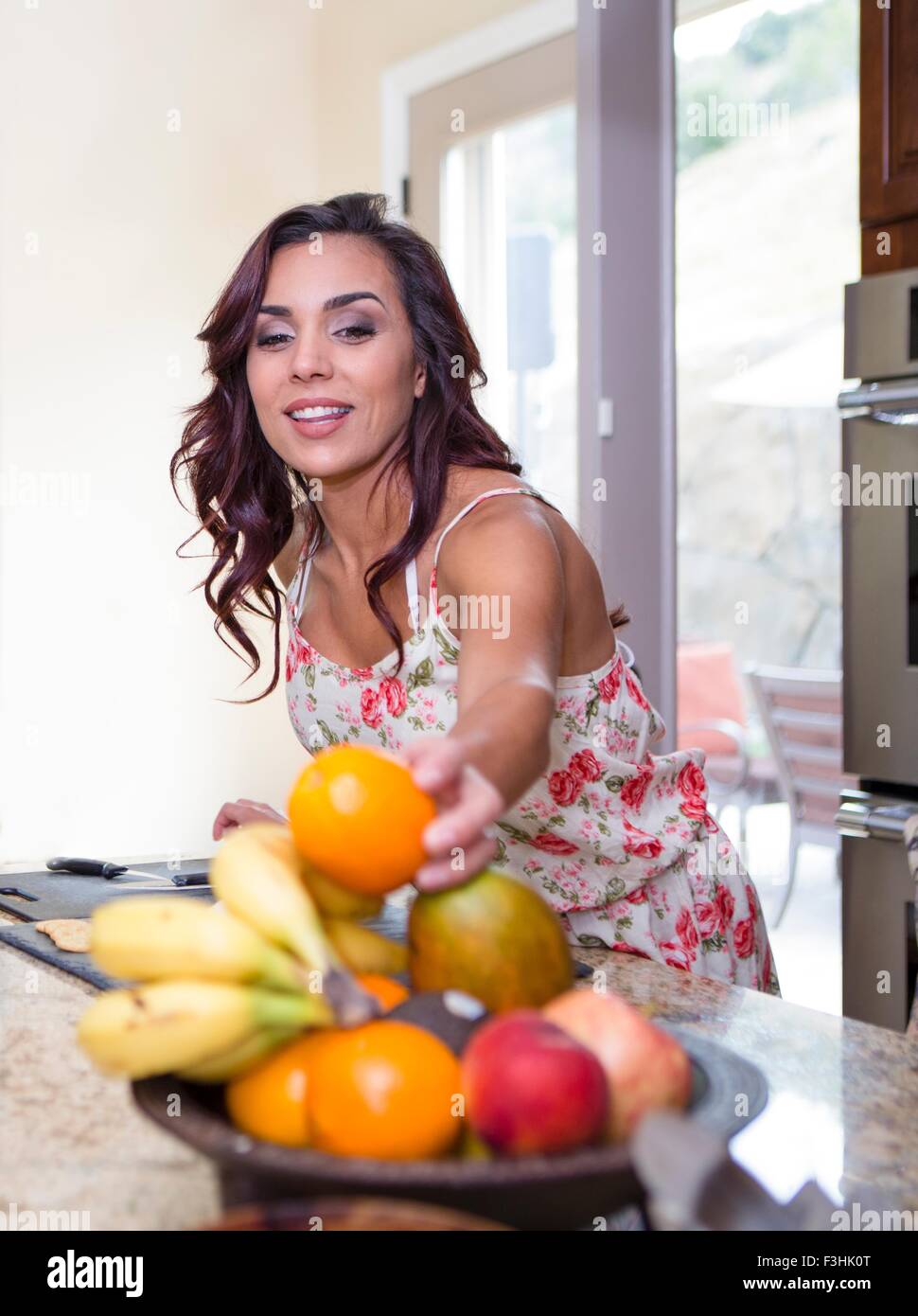 Mid adult woman picking up orange from fruit bowl Stock Photo