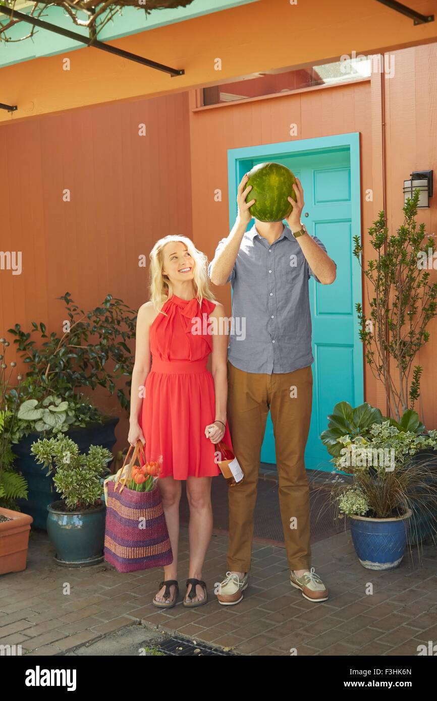 Woman with bottle of wine and man covering face with watermelon Stock Photo