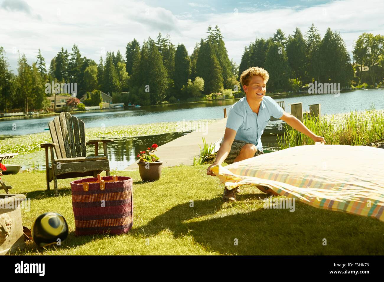 Man laying picnic blanket on grass, lake in background, Seattle, Washington, USA Stock Photo