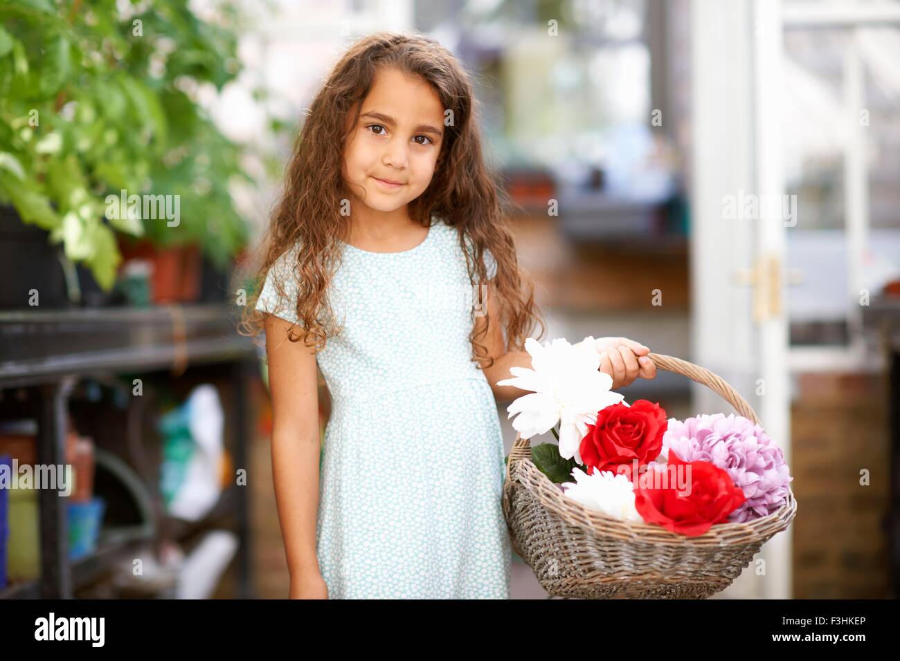Cute girl holding basket of fresh flowers in greenhouse Stock Photo