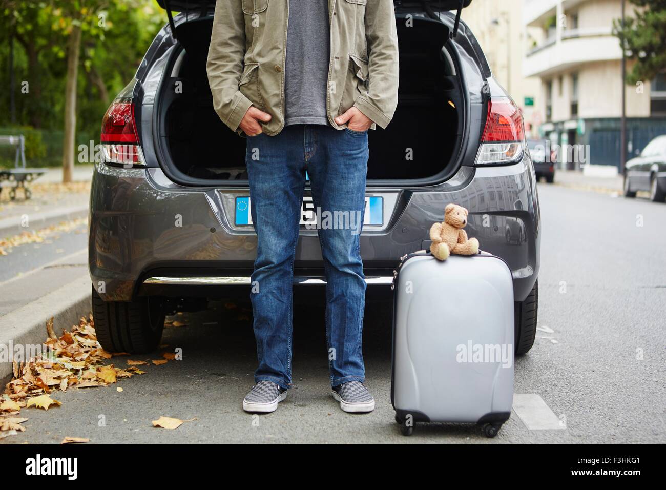 Mid adult man standing beside car with open boot, suitcase in road Stock Photo