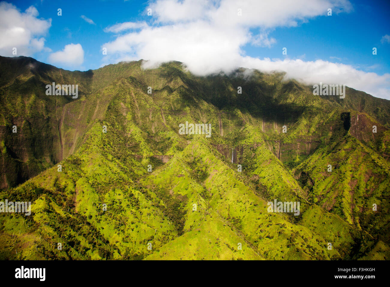 KAUAI, HAWAII, USA. Aerial image of lush green mountain slopes under soft clouds and blue sky. Stock Photo