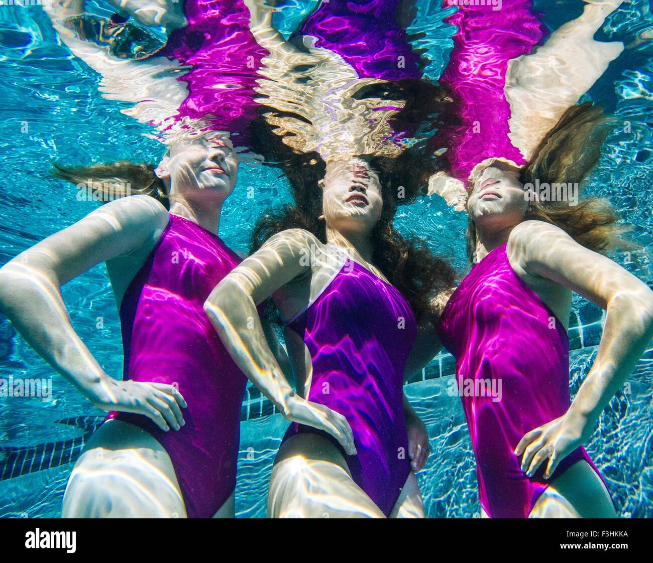 Three female swimmers, underwater, hands on hips Stock Photo