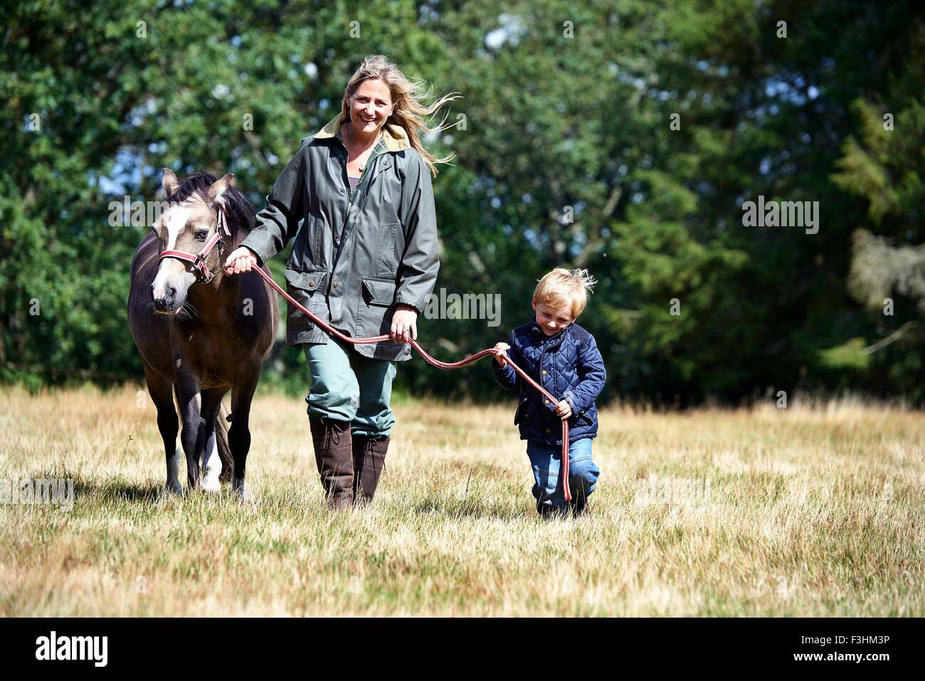 Mother and son walking pony in field Stock Photo