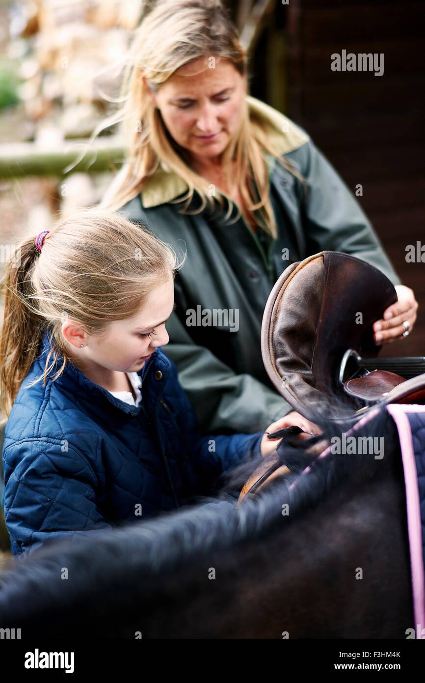 Mature woman and daughter saddling horse Stock Photo