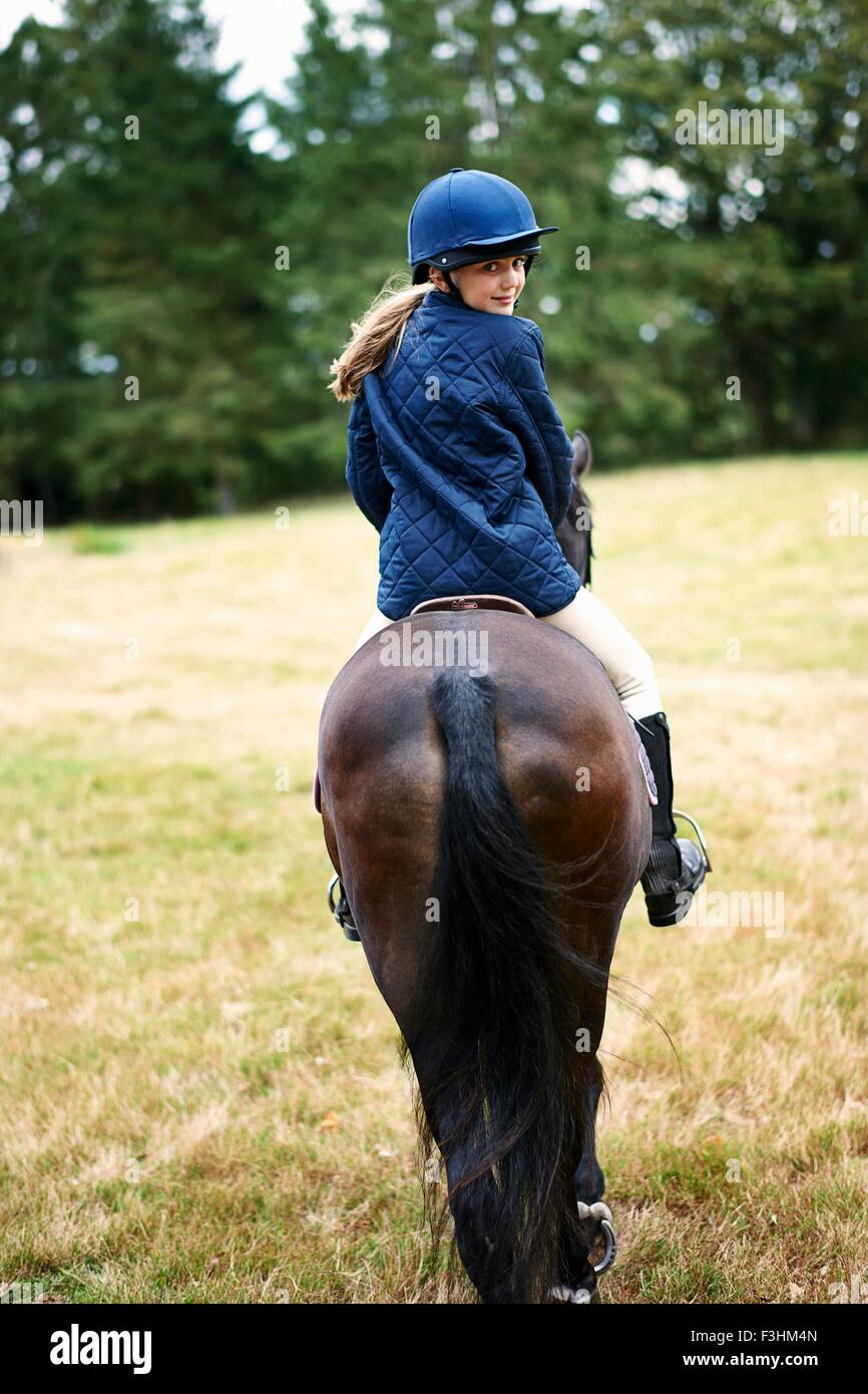 Rear view of girl horseback riding in field Stock Photo