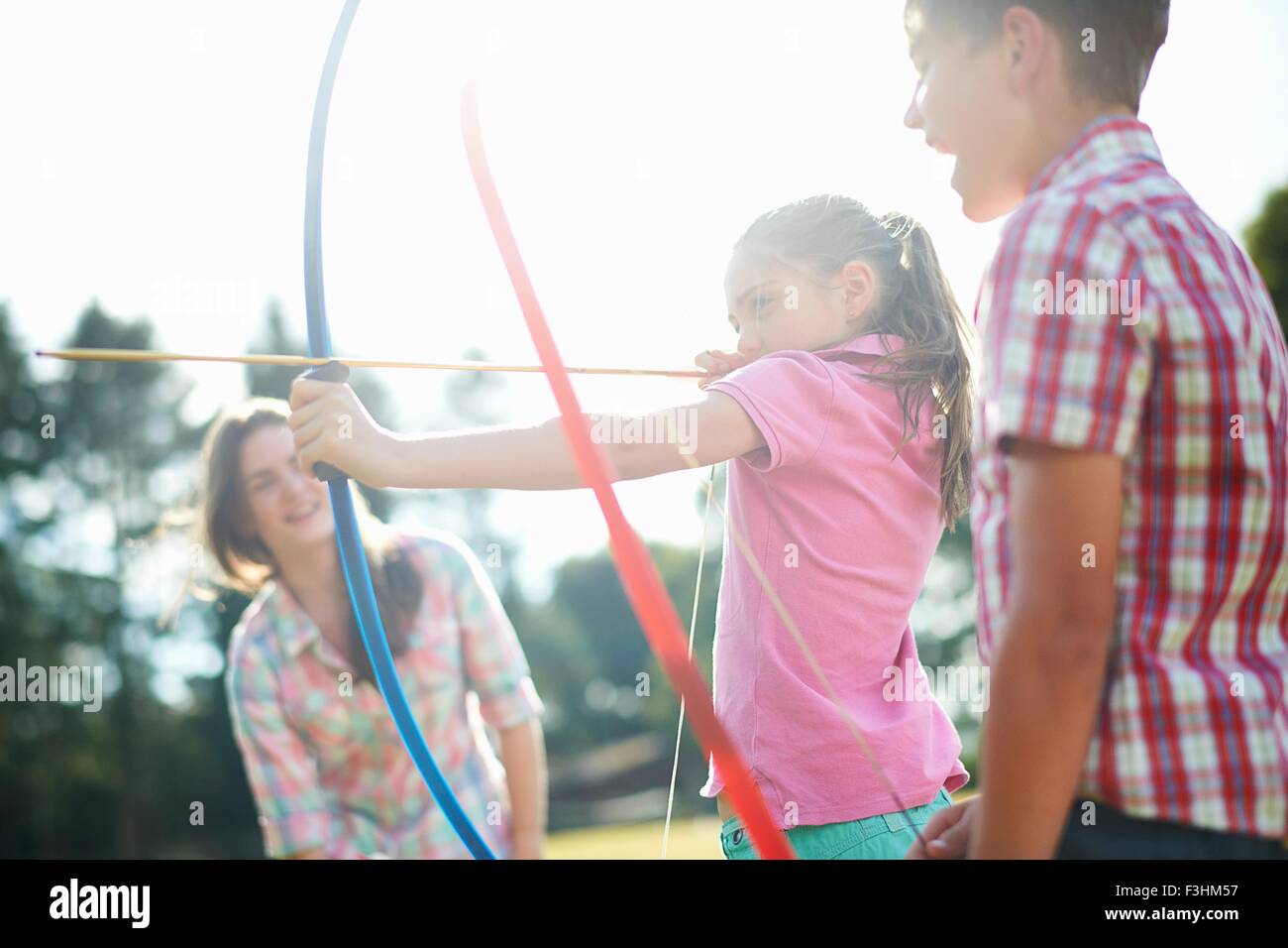 Girl learning archery from teenage sister and brother Stock Photo