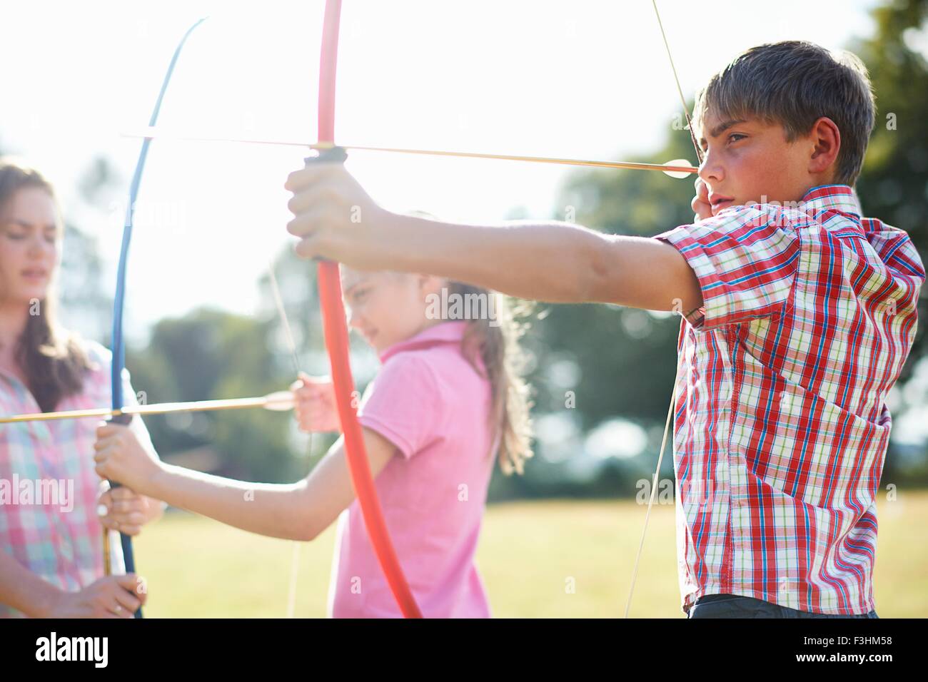 Girl practicing archery with teenage sister and brother Stock Photo