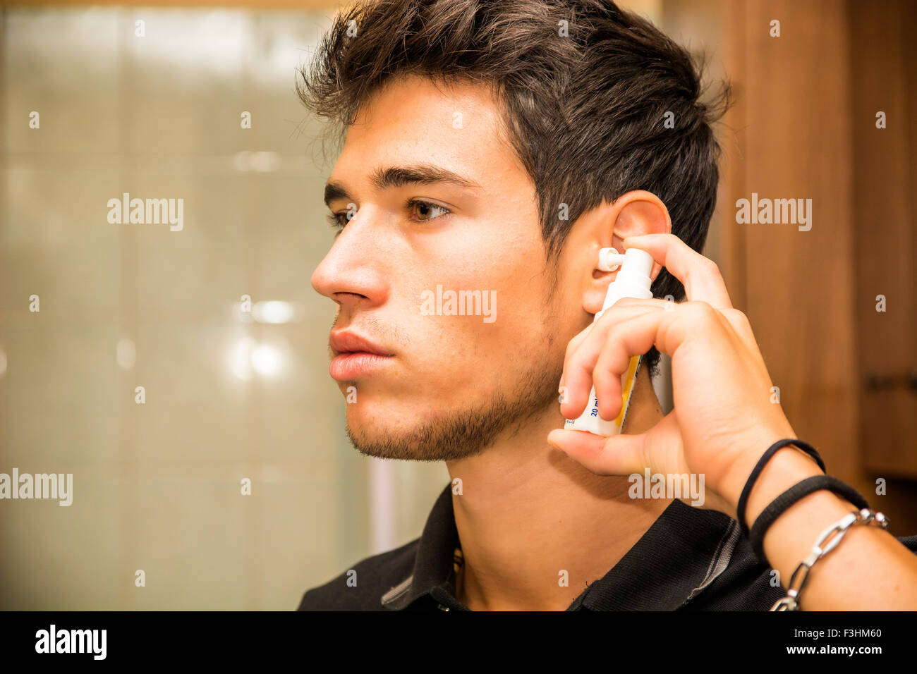 Head and Shoulders Close Up of Attractive Young Man with Dark Hair Spraying Ear Spray into Ears as part of Morning Grooming Rout Stock Photo