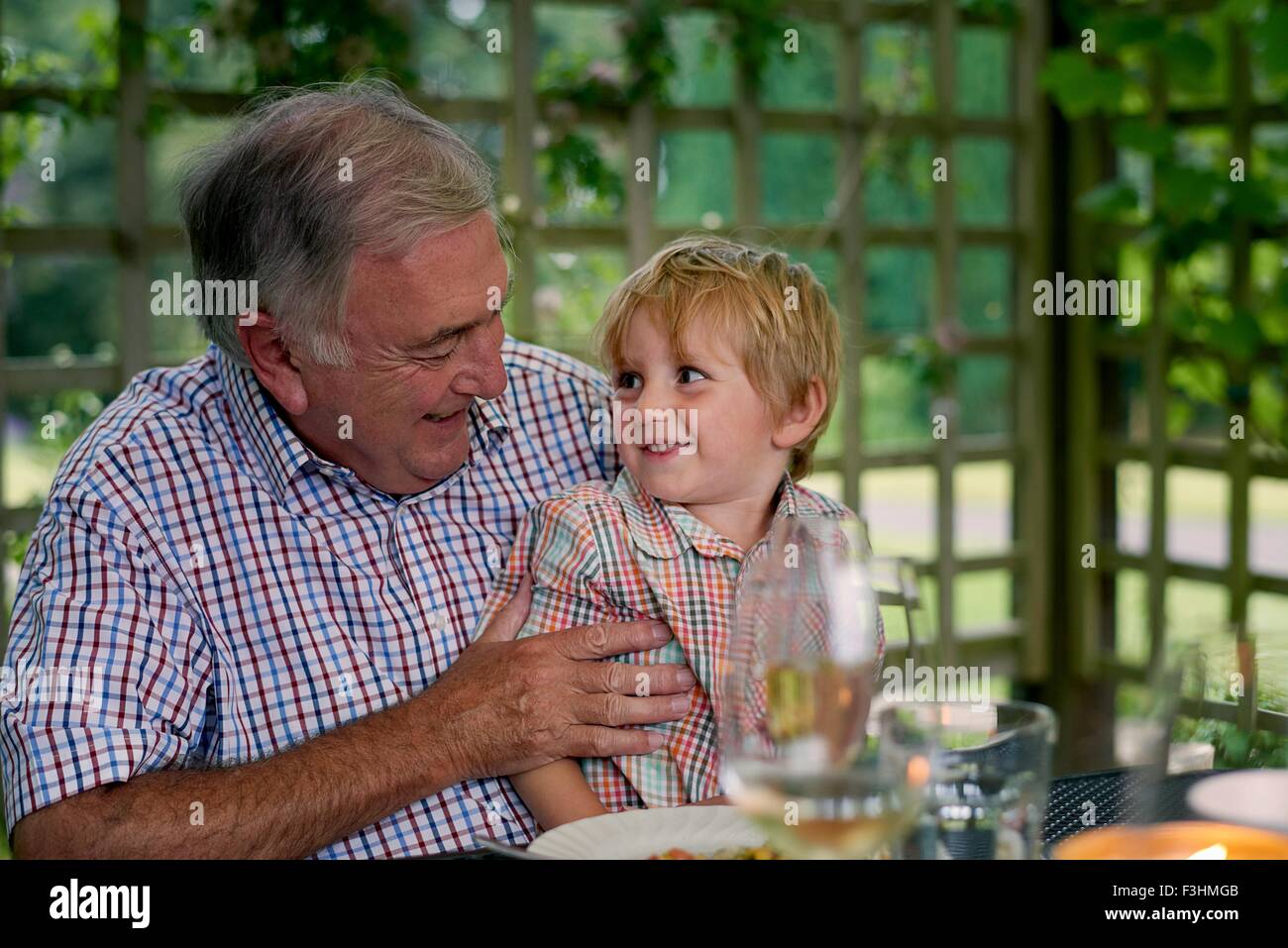 Grandson sitting on grandfathers lap, face to face smiling Stock Photo