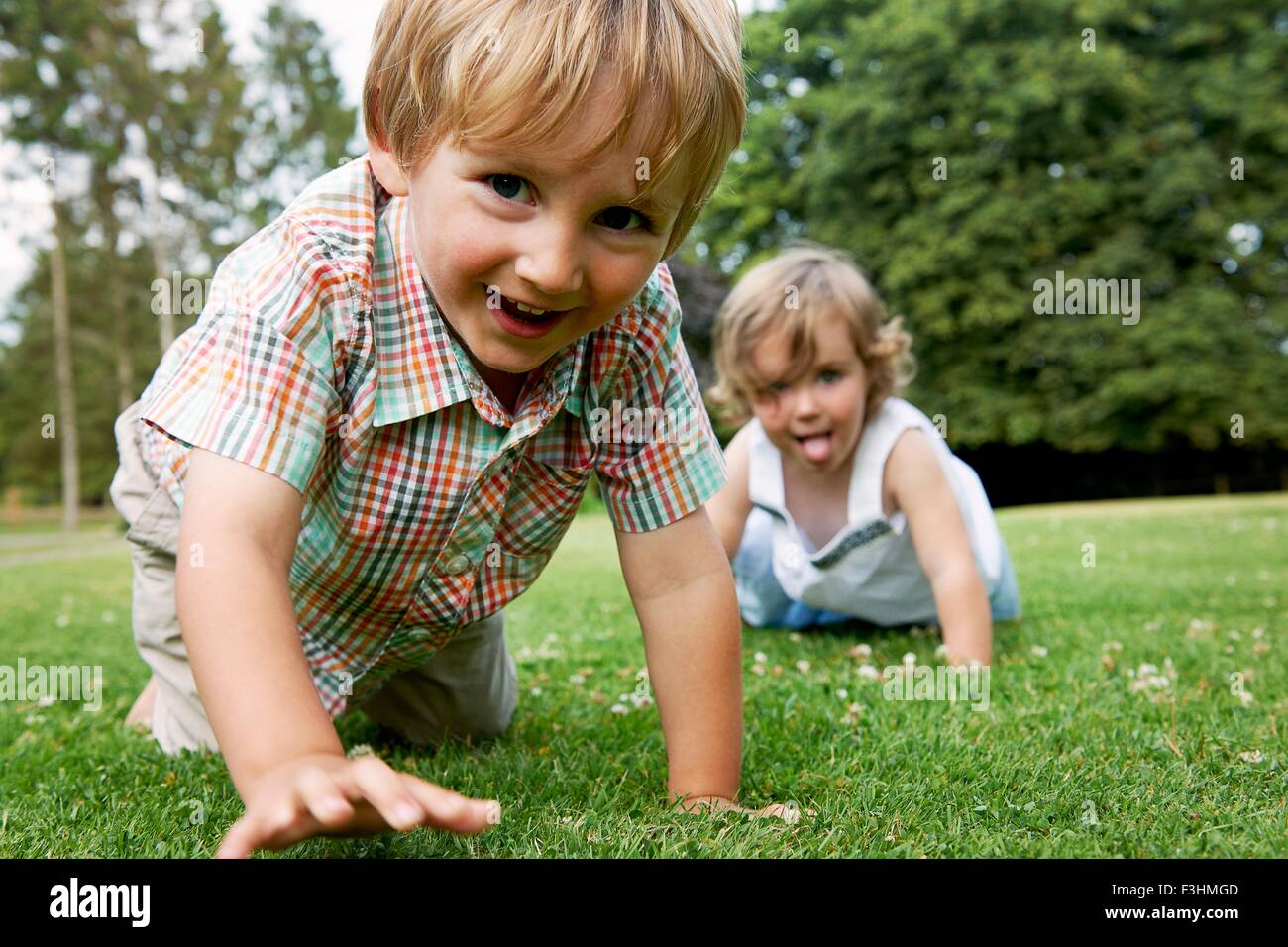 Boy and girl on grass crawling on hands and knees, looking at camera smiling Stock Photo