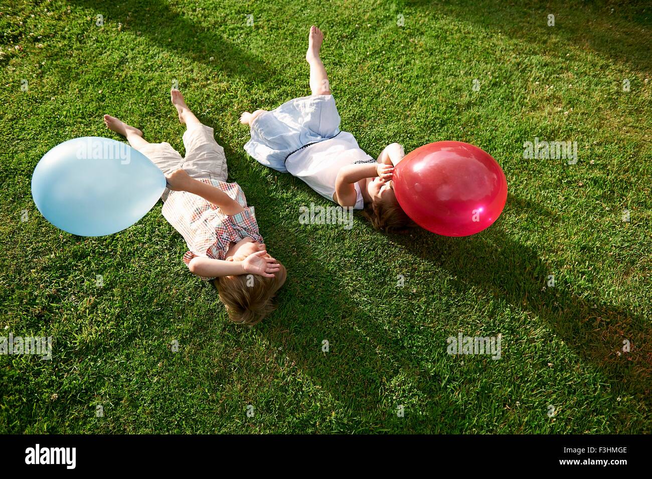 High angle view of brother and sister lying on grass holding balloon Stock Photo