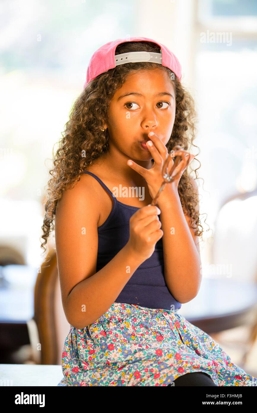 Girl holding whisk licking cake mix off fingers looking away Stock Photo