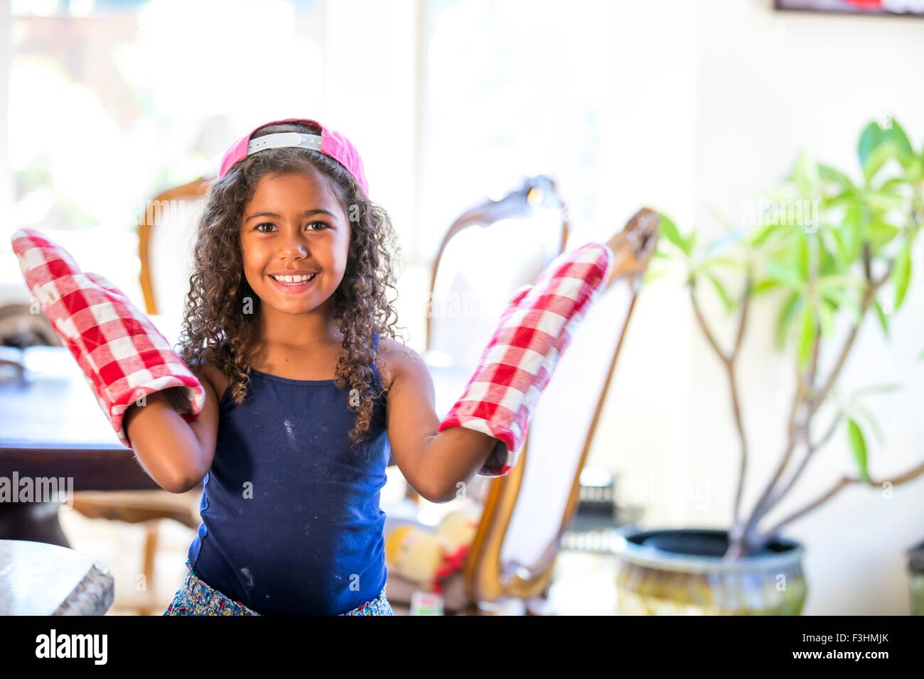 Girl wearing oven gloves hands raised looking at camera smiling Stock Photo