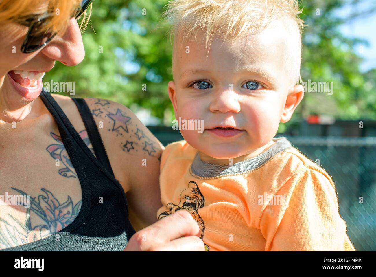 Head and shoulders of tattooed mother holding baby boy looking at camera Stock Photo