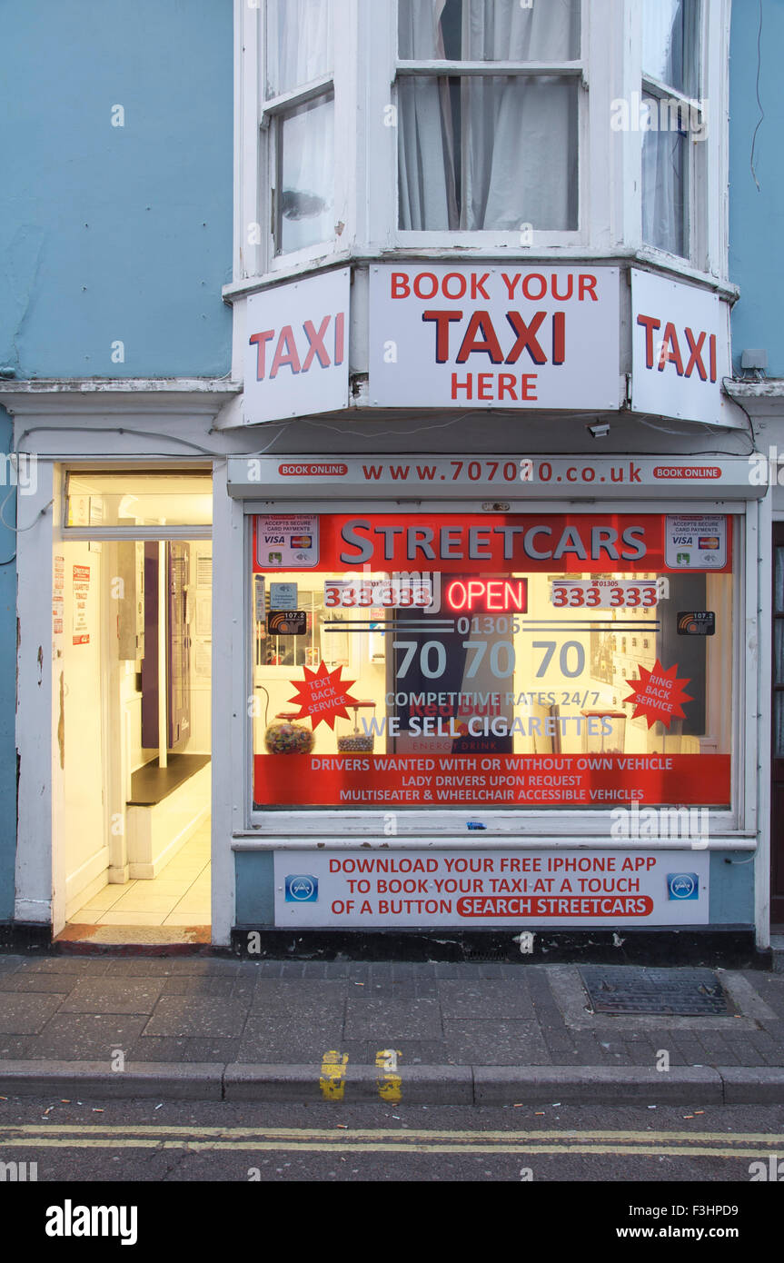 'Book your Taxi here'. The bright evening lights and advertising signs of the 'Streetcars' Taxi company office. Weymouth, Dorset, England, UK. Stock Photo