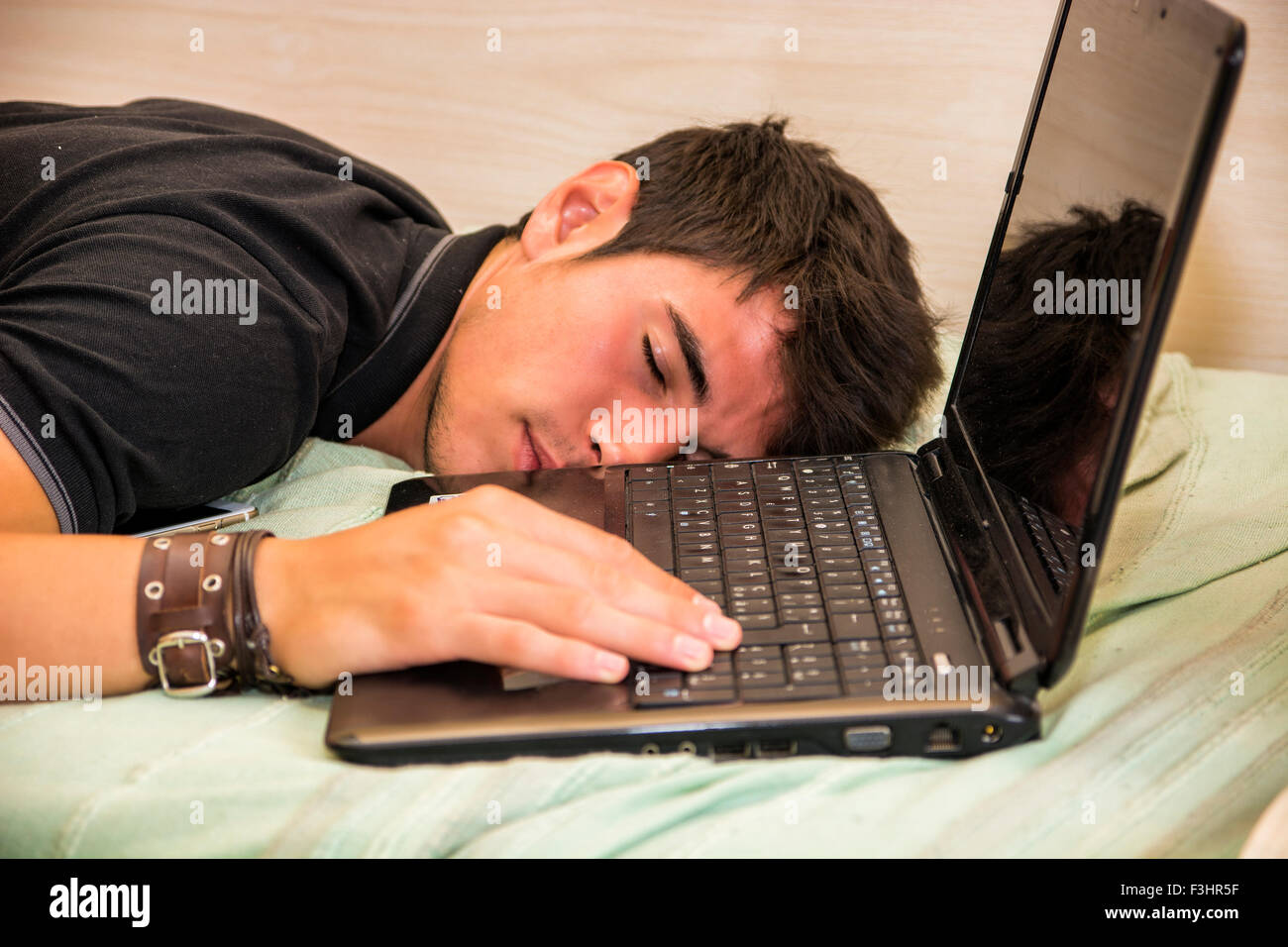 Close Up of Tired Young Man with Dark Hair Sleeping on Floor Next to Laptop Computer with Hand on Keyboard Stock Photo