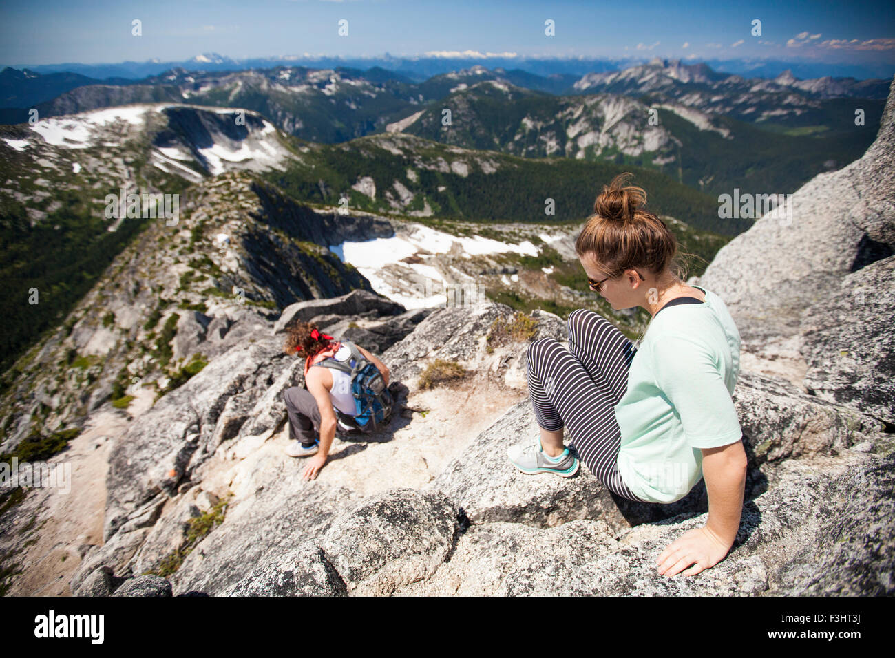 A young couple scramble down granite rock on the summit ridge of Needle Peak. Stock Photo