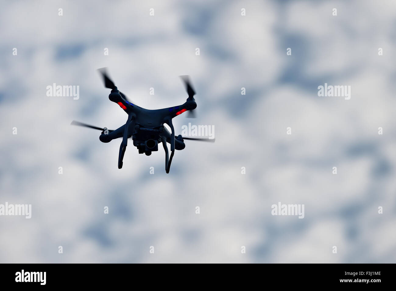 Aerial filming drone in action, silhouetted against blue cloudy sky Stock Photo