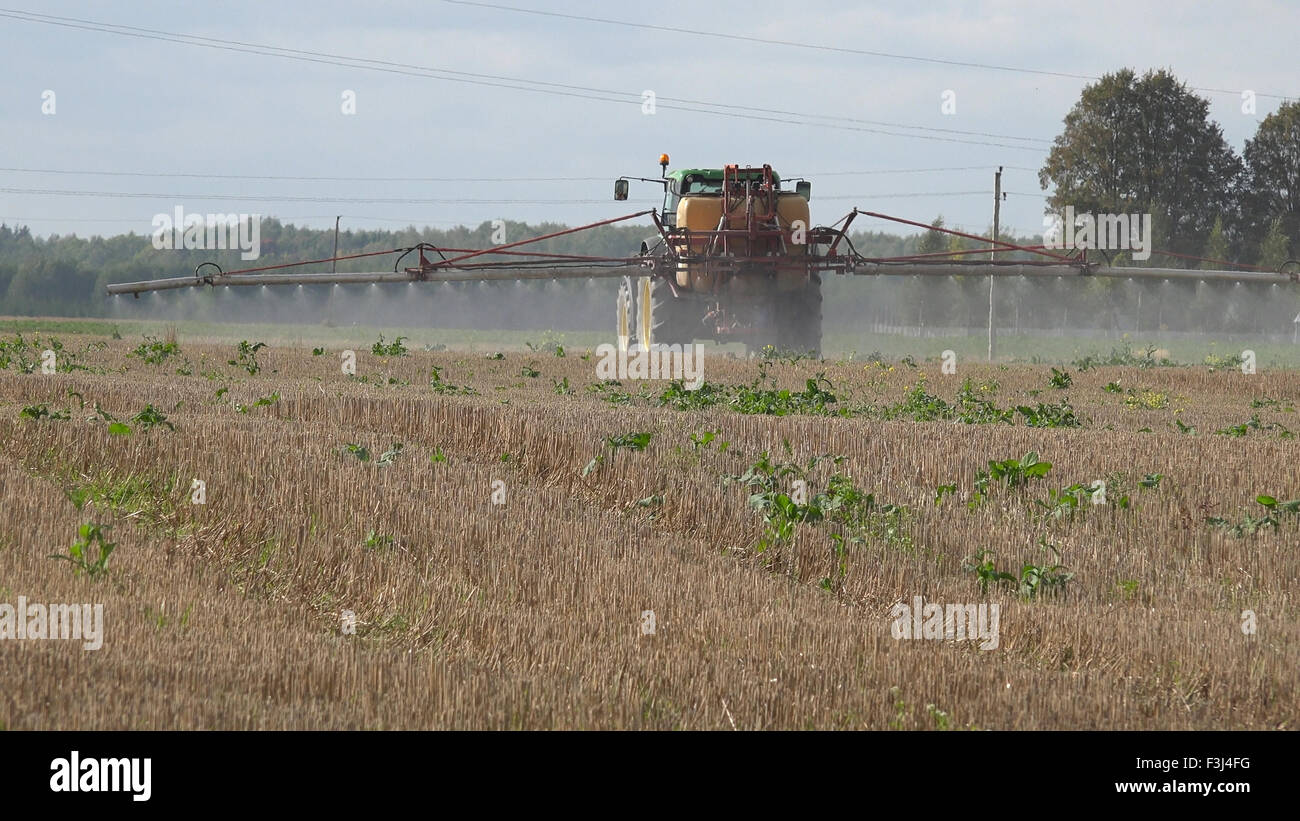 Tractor spray stubble field with herbicide chemicals in autumn. Farmer killing weeds in agriculture field before winter. Stock Photo